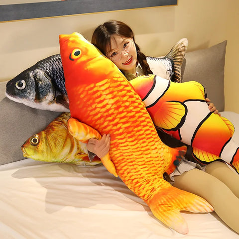 A person on a bed holding the orange red carp pillow, with the grass carp, crucian carp and clownfish piled beside it - one fish per order