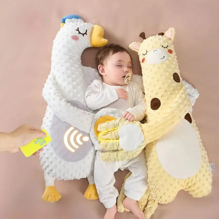 A baby lying between the white goose and the yellow giraffe pillow, with a hand holding the small remote at the edge of the frame