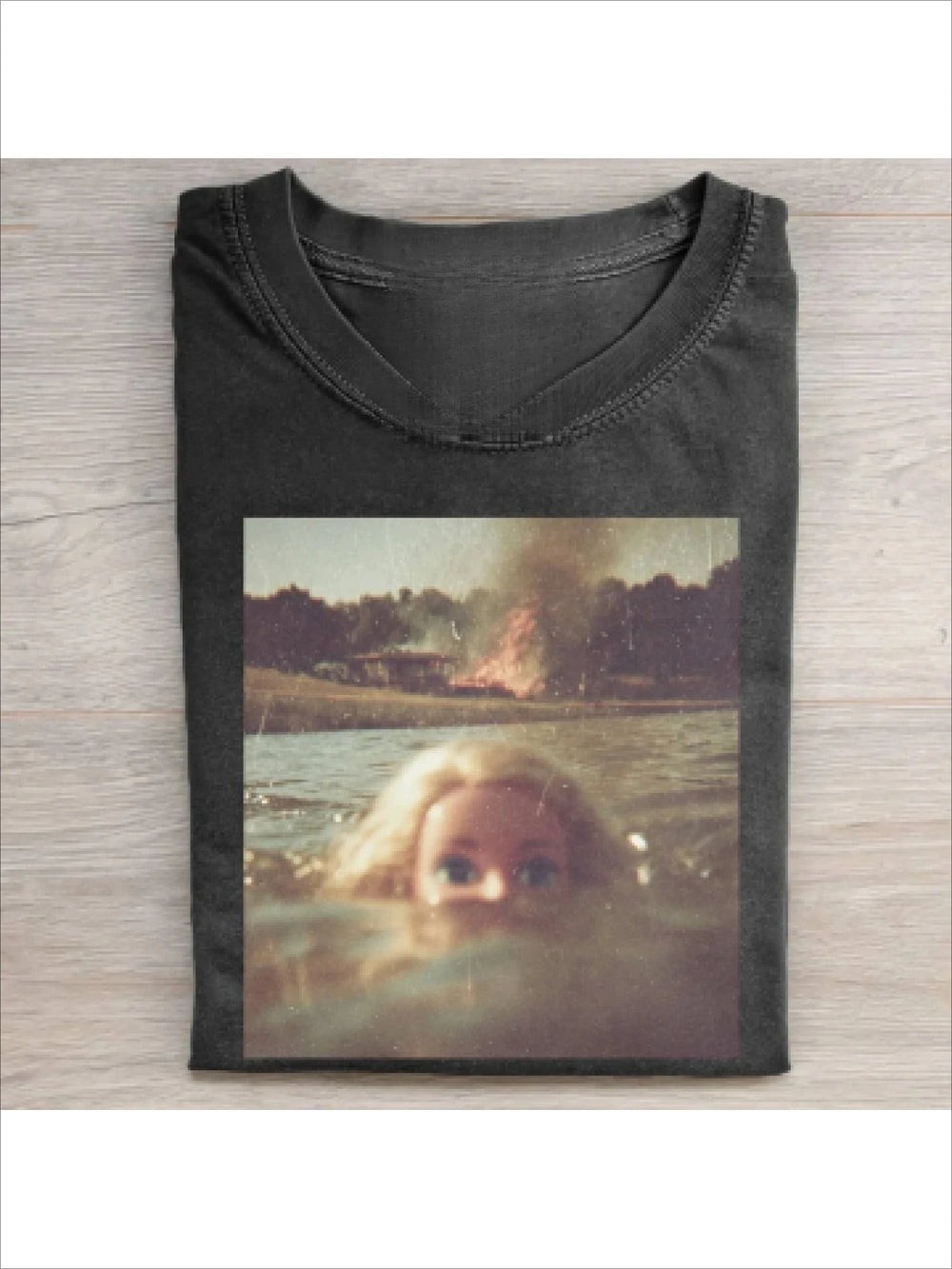 Washed black tee printed with a faded photograph of a blonde doll head half submerged in a lake, a building burning on the far shore