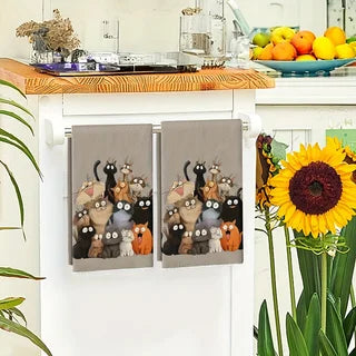 The pair of cartoon cat towels hanging from a white oven door rail in a kitchen, fruit bowl and sunflower nearby