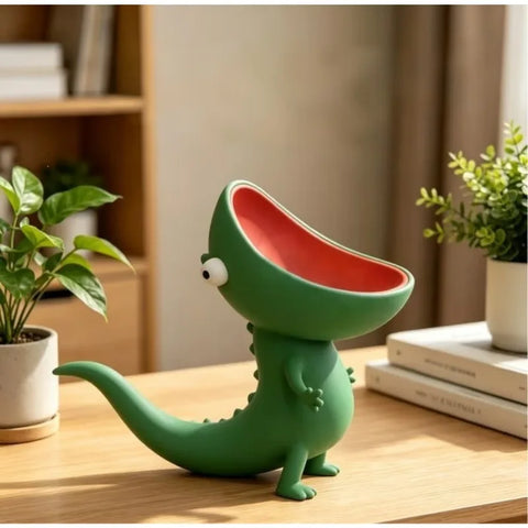 Green resin lizard soap dish on a wooden desk beside houseplants, head tipped back so its open mouth forms a coral-red bowl