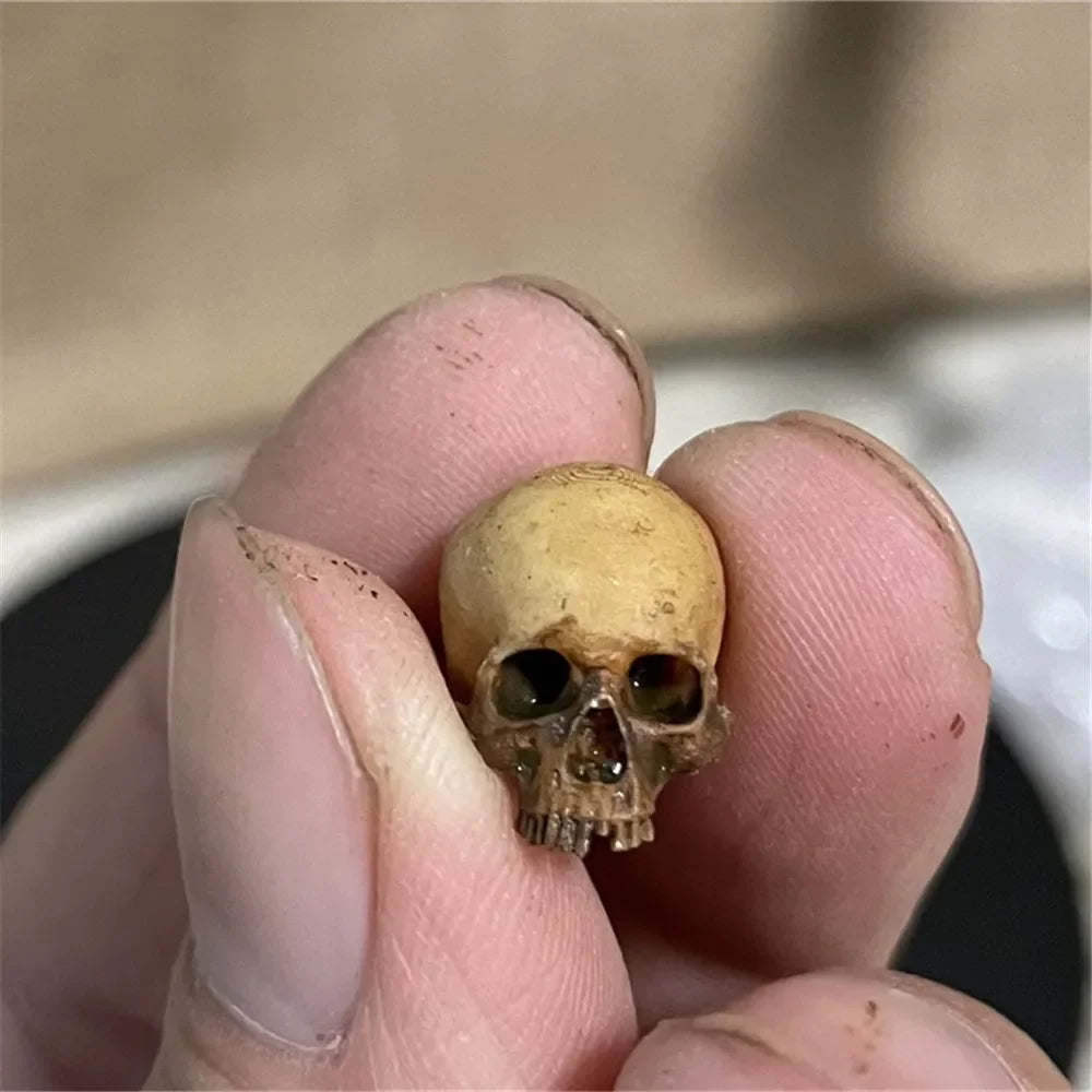 Aged Bone: the miniature skull with a darkened, weathered finish, held between finger and thumb