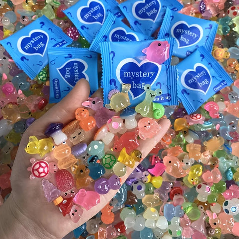 A hand holding several sealed blue mystery bags above a pile of tiny coloured figures