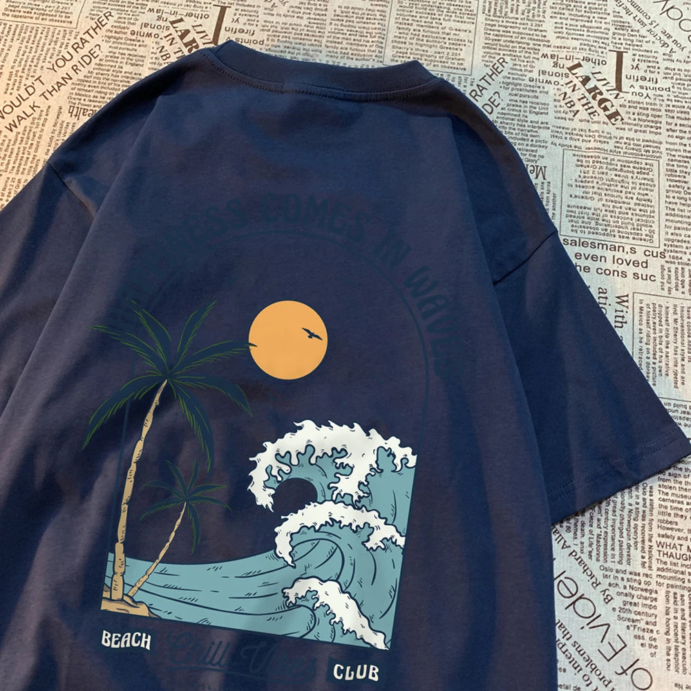 Navy cotton tee with a large back print of a breaking wave, palm trees and a low sun, under the arched words Happiness Comes In Waves