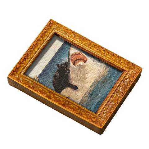 Carved gold frame magnet holding a painting of a black cat riding an open-mouthed shark