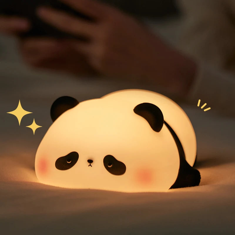 The sprawled panda night light lying chin-down on a bed sheet and glowing warm, seen from the front