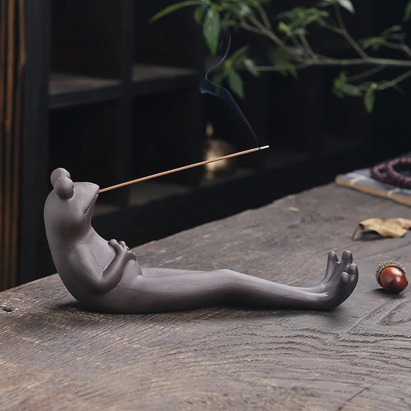 The frog holder on a wooden table with smoke rising from the stick