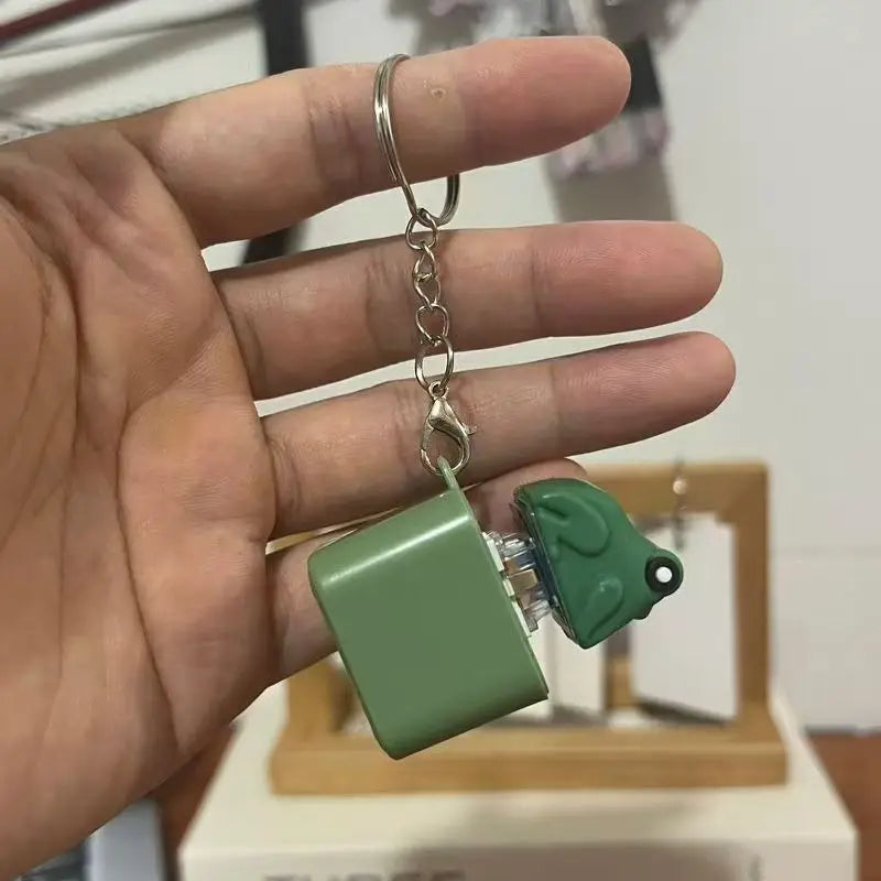 The green frog keychain lying across an open palm, split ring and lobster clasp extended