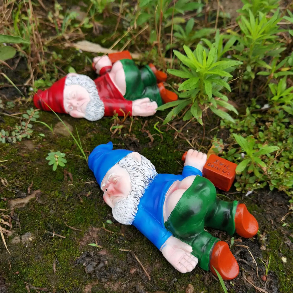 Two of the gnomes lying in a garden border among plants