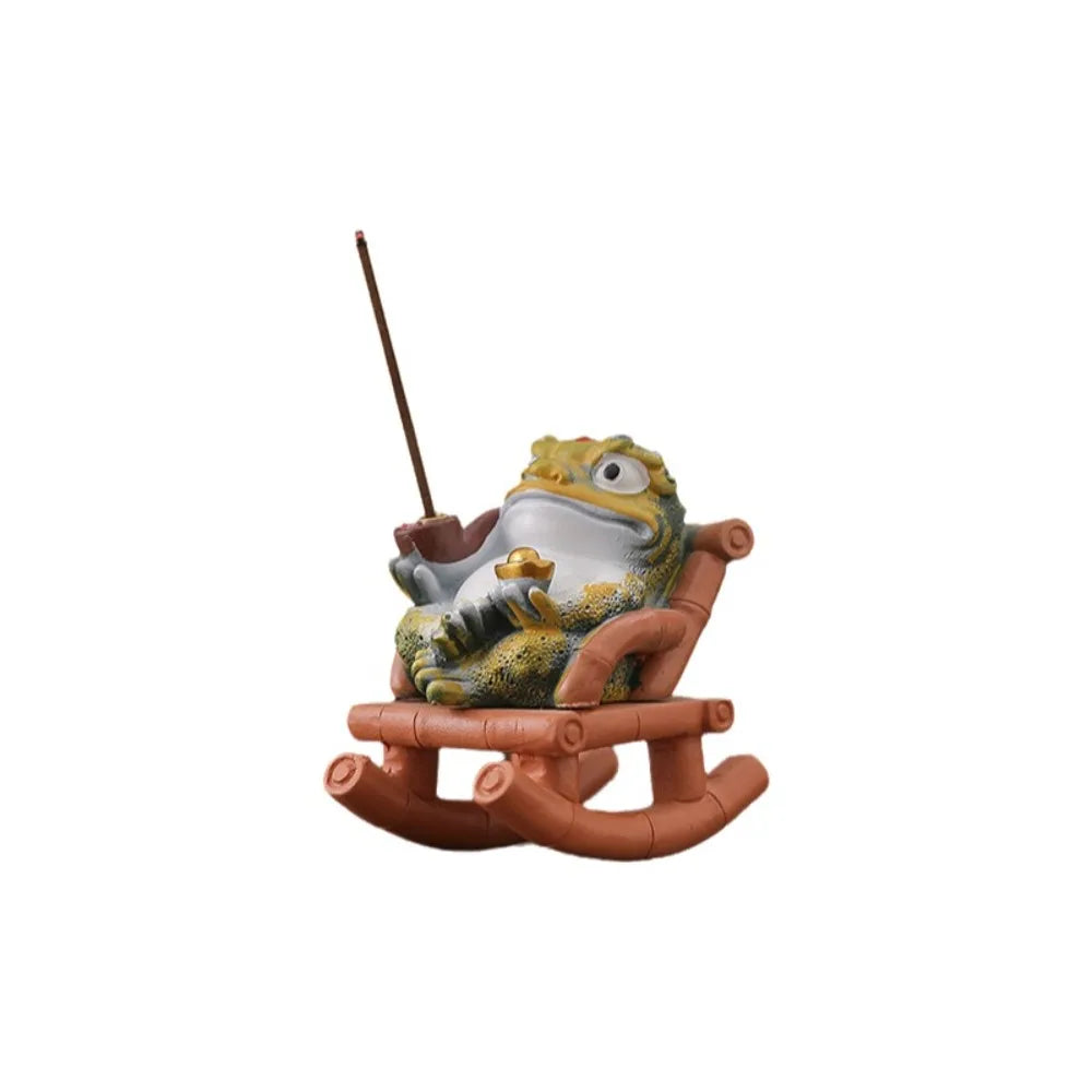 Painted resin toad reclining in a small rocking chair with an incense stick behind