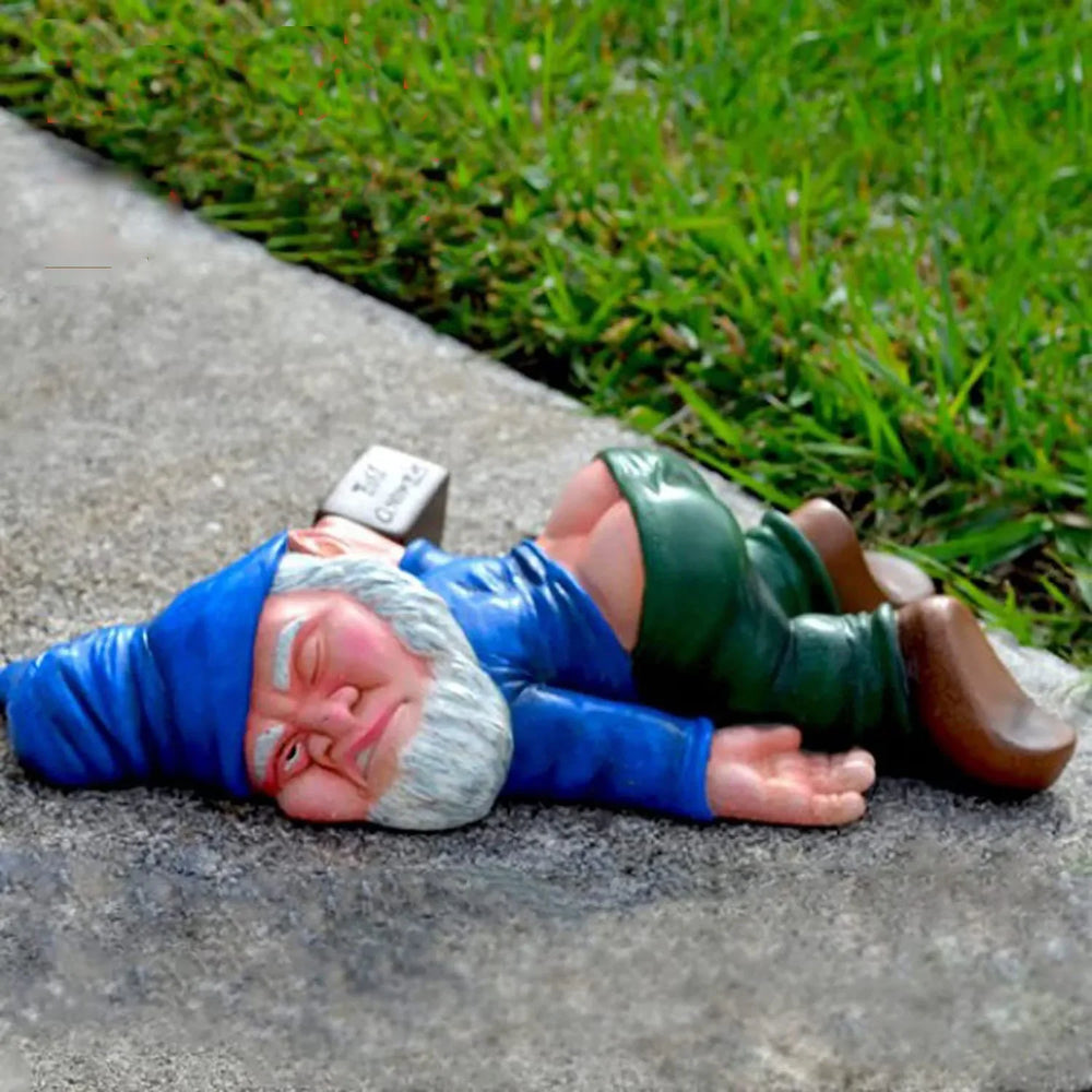 A blue-coated gnome lying face down on a stone edge beside grass