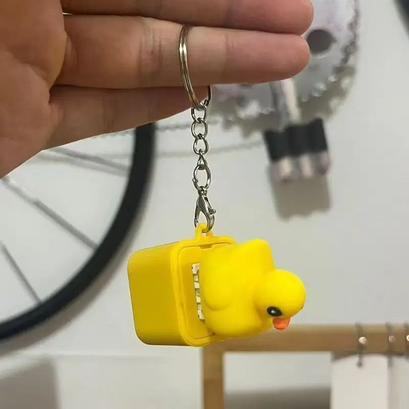 The yellow duck keychain held in a hand by its split ring and chain, showing its size against the fingers