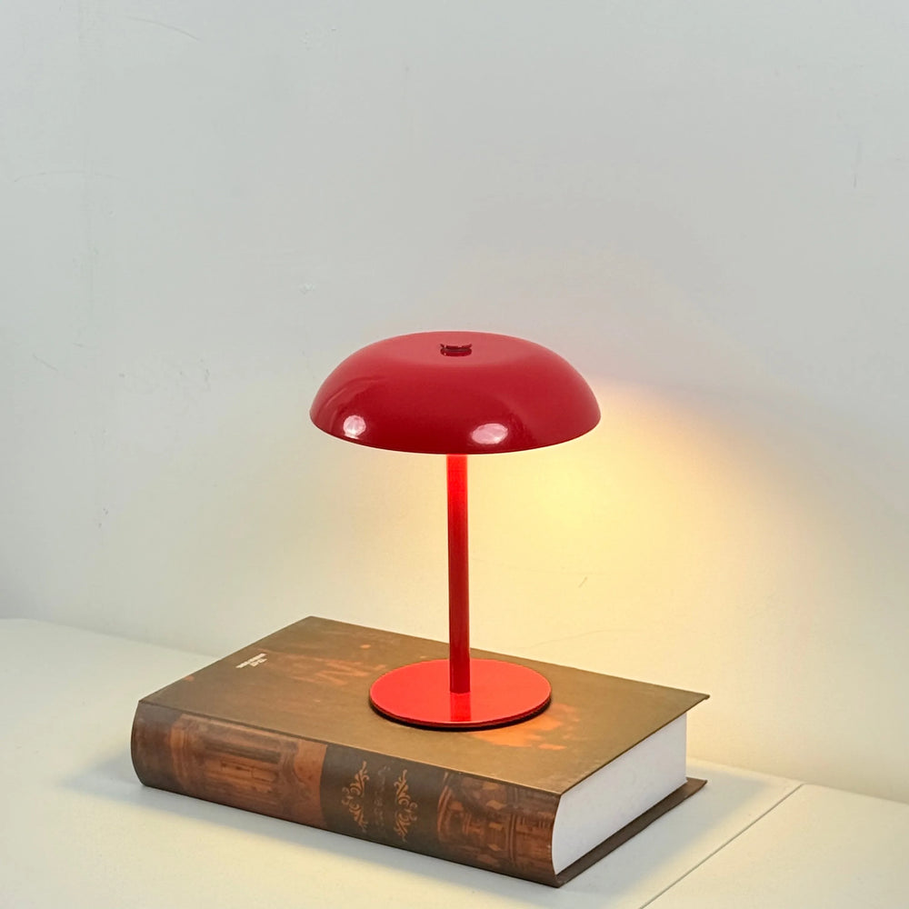 The lamp in the red finish, lit warm on a hardback book
