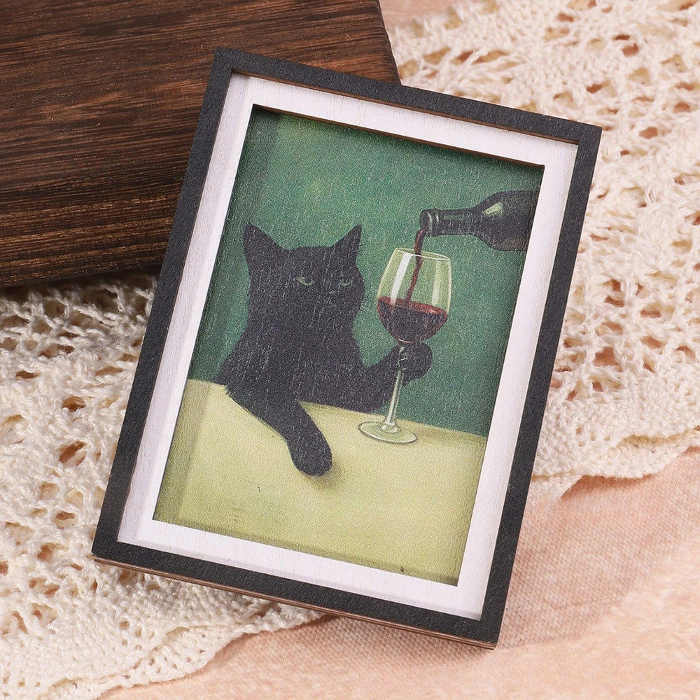 The framed cat and wine magnet propped at an angle to show the black moulding