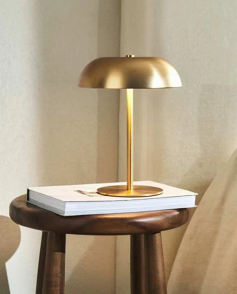 Gold mushroom-dome table lamp lit on a book on a dark wooden stool