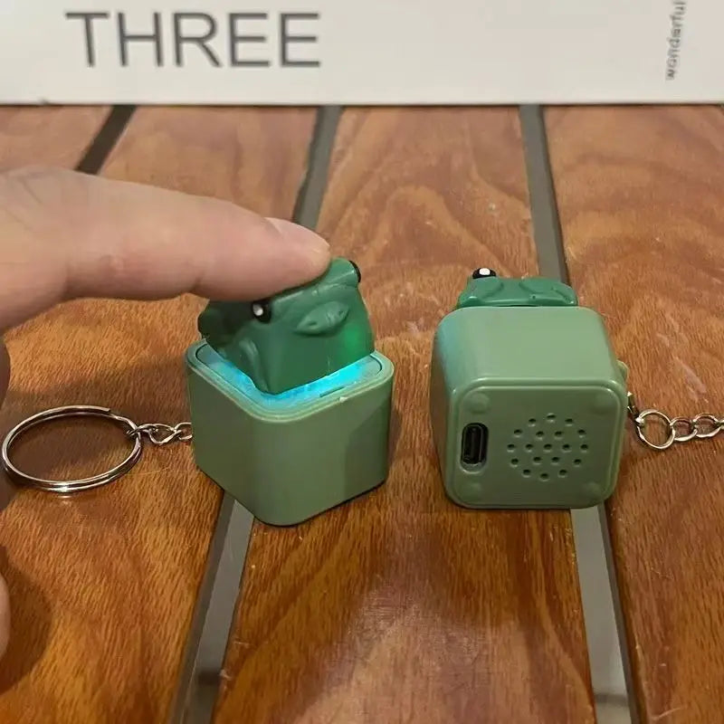 A finger pressing the frog keycap so the blue LED lights beneath it, with the second unit turned to show its USB-C port and speaker grille