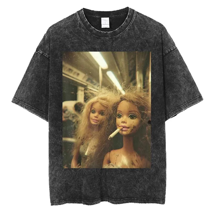 Washed charcoal tee laid flat, printed with a photograph of two dishevelled fashion dolls on a subway train, one holding a lit cigarette in her mouth