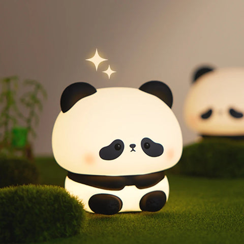 The sitting panda night light glowing warm white on moss beside a bamboo shoot, a second one blurred behind it