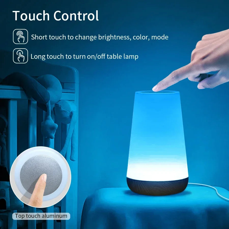 A finger pressing the round touch pad on top of the lamp, which is glowing blue beside a cot