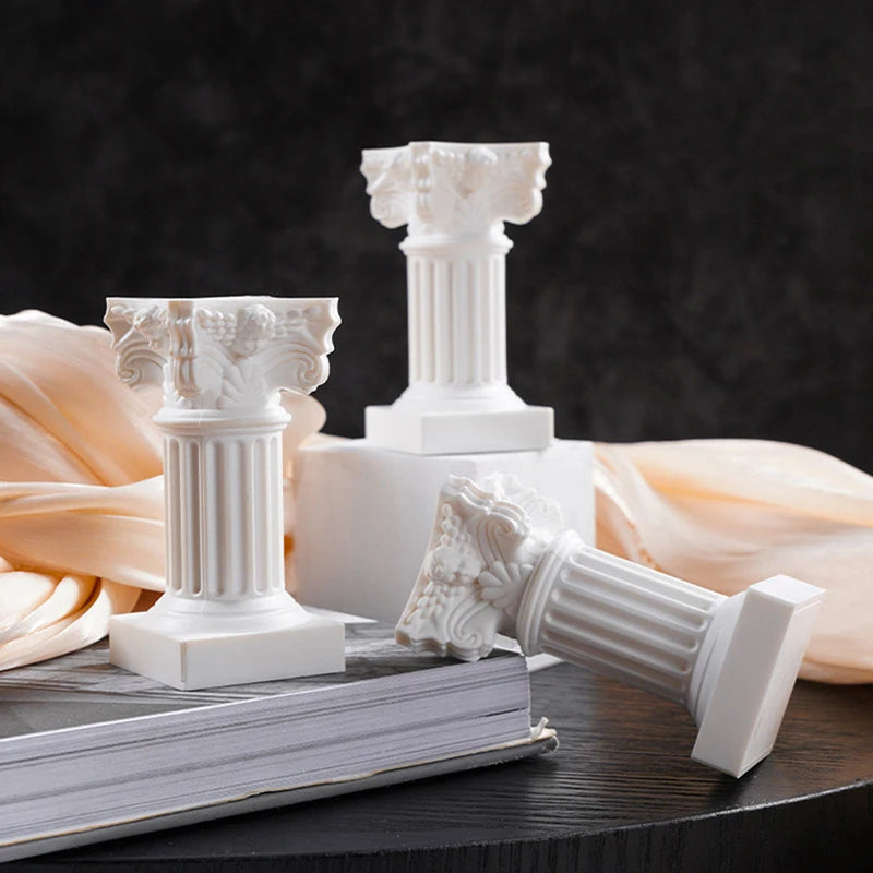 Three white column candle holders on a stack of books, one lying on its side