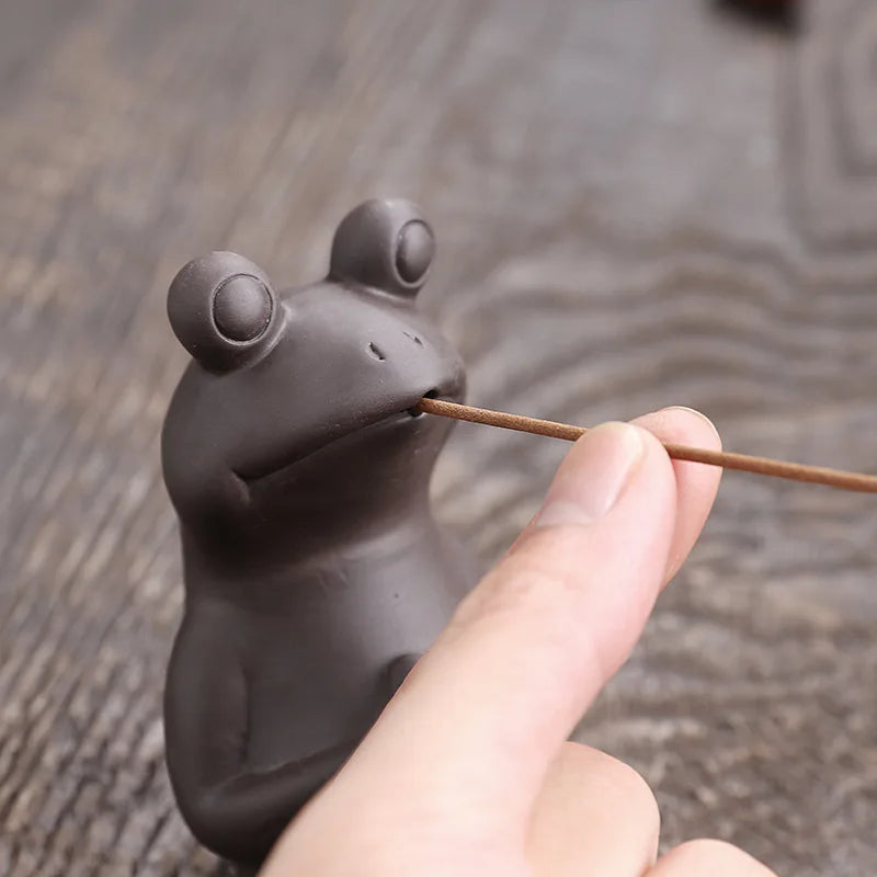 Close-up of the frog's face gripping the incense stick