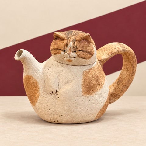 Orange and cream rustic cat-shaped teapot on a cream and burgundy studio background