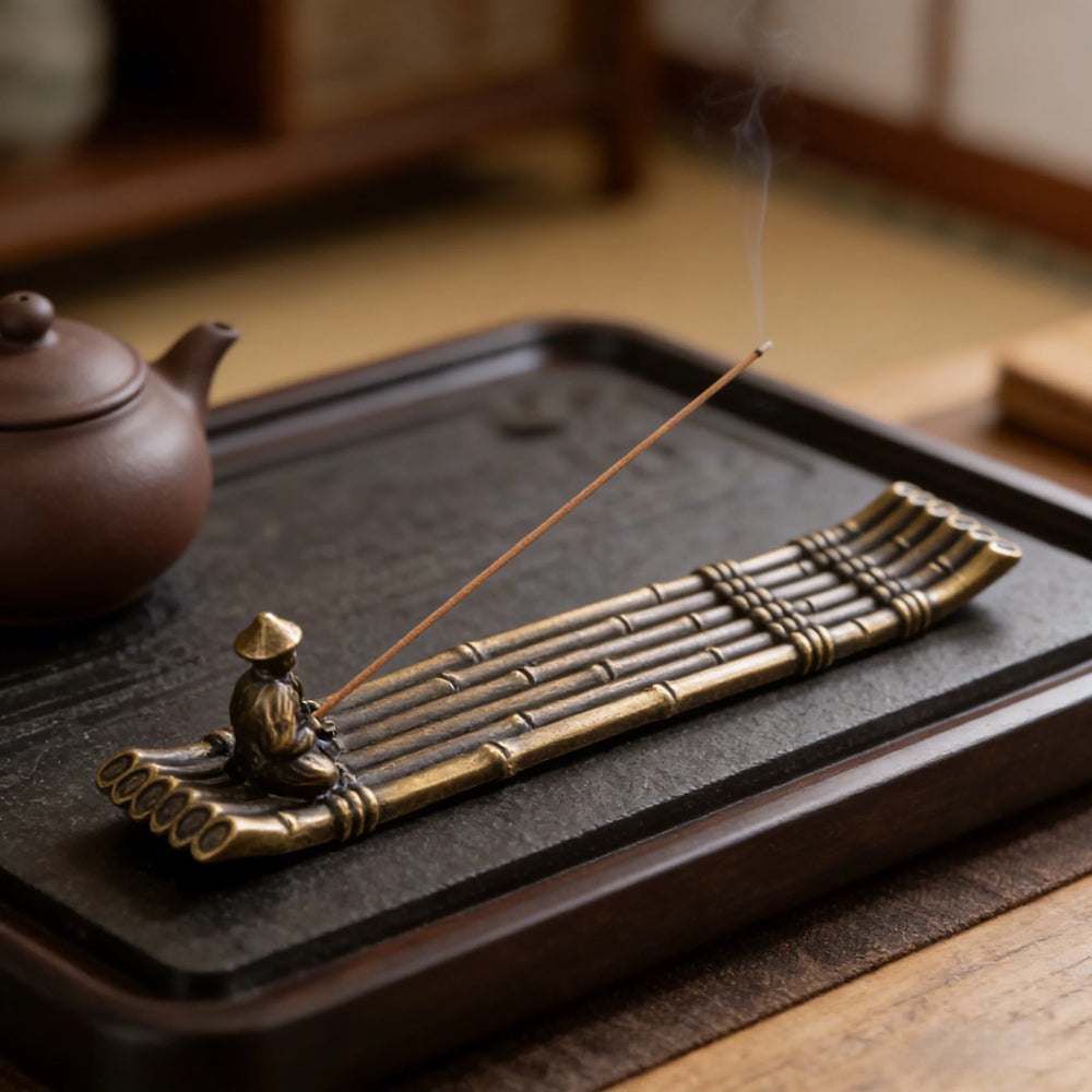Metal bamboo-raft incense holder with a tiny fisherman, lit stick, on a tea tray