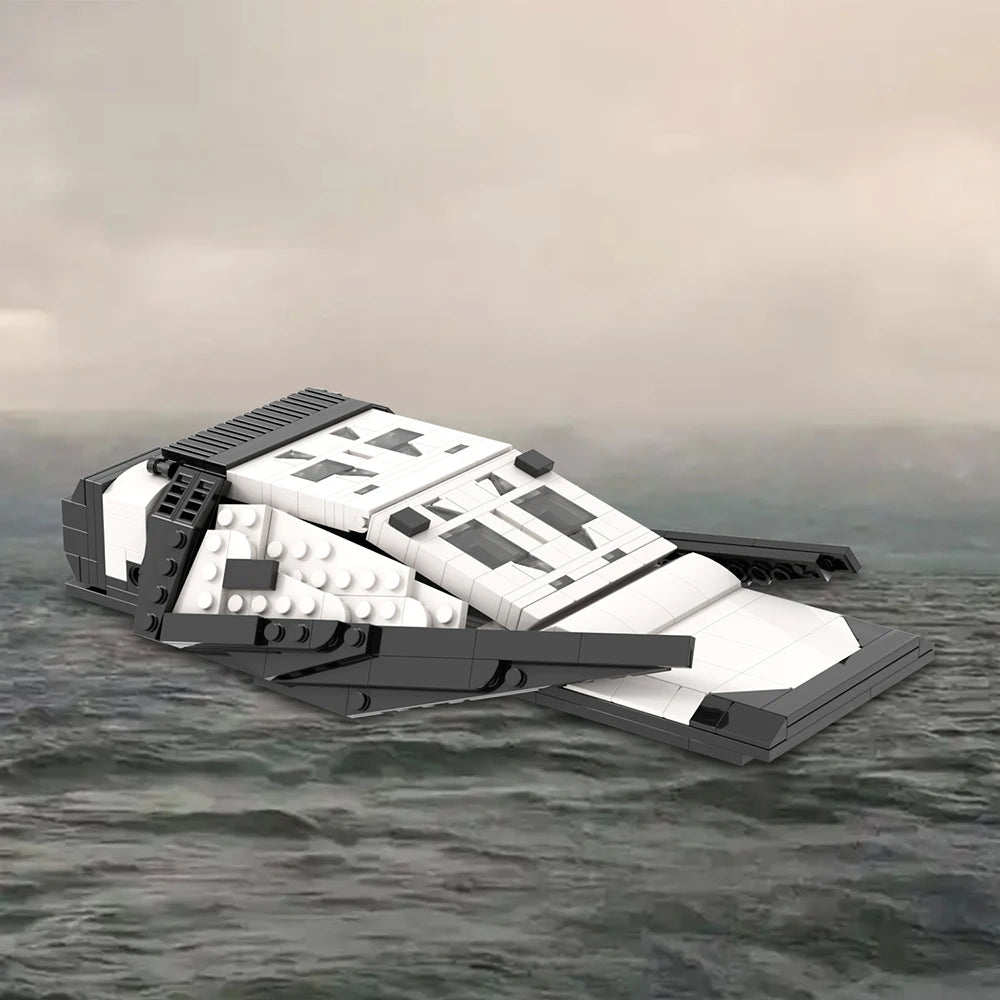 White and dark grey brick built spacecraft with twin cockpit windows and four low swept wing plates, photographed against a grey sea and sky