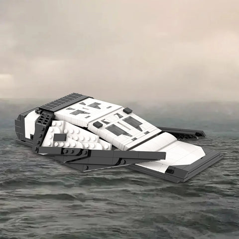 White and dark grey brick built spacecraft with twin cockpit windows and four low swept wing plates, photographed against a grey sea and sky