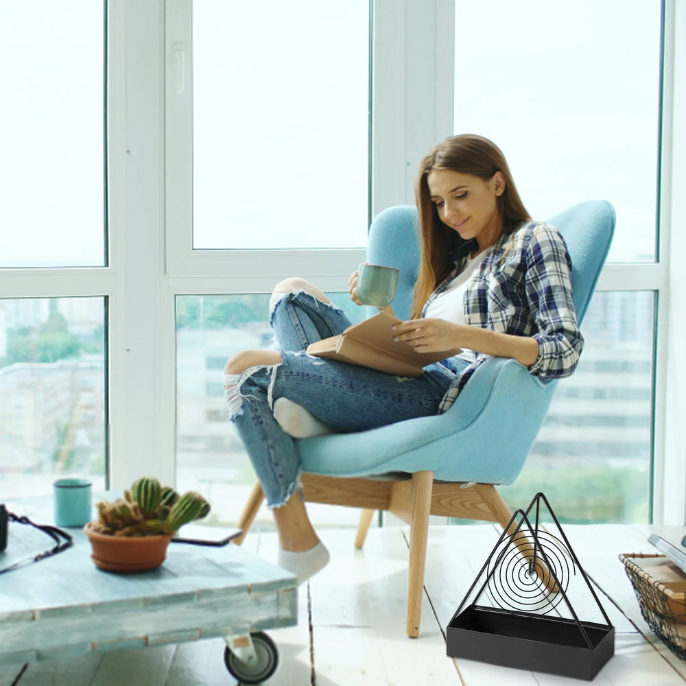 A black holder with a coil on the floor beside a chair - the furniture, mug and potted plant are not included