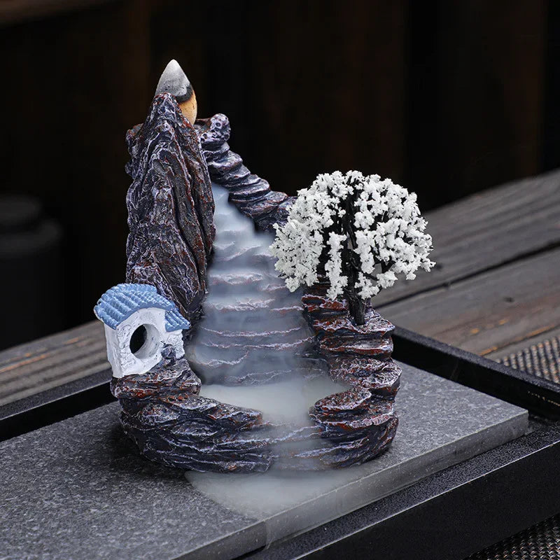 Backflow incense burner with white blossom tree and blue cottage, smoke running down the waterfall