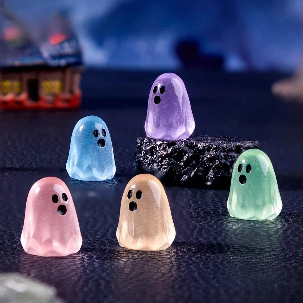 Five small glow-in-the-dark resin ghosts in pink, blue, purple, green and orange on a dark surface