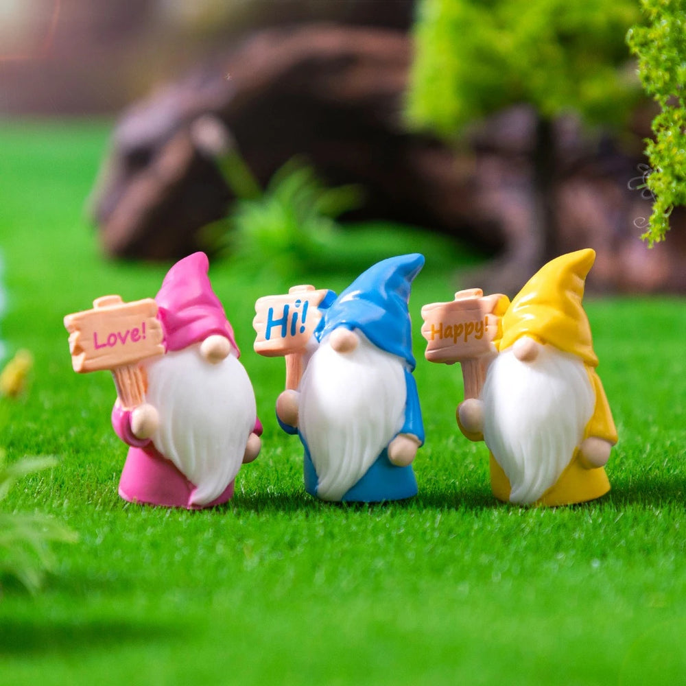 Close-up of three gnomes in pink, blue and yellow pointed hats holding signs reading Love, Hi and Happy