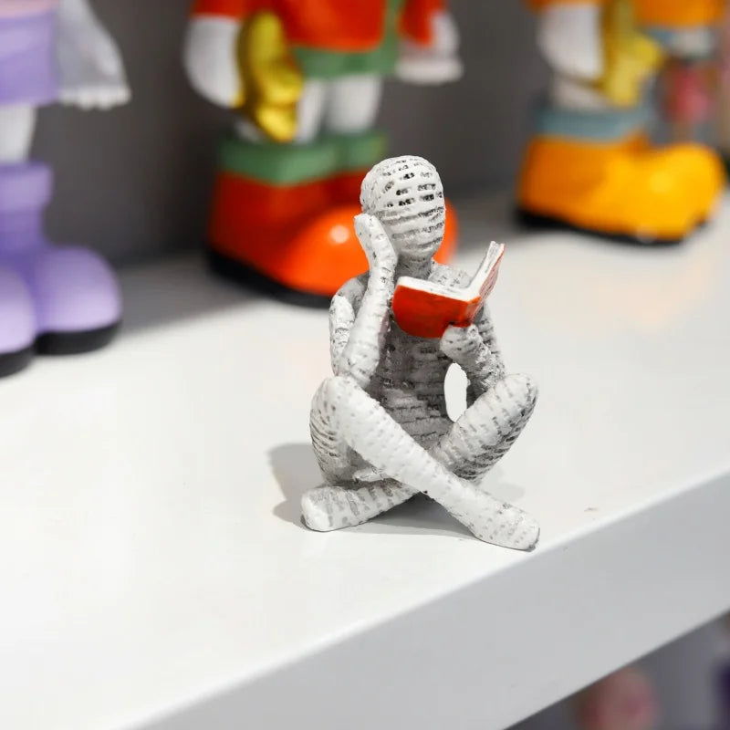 The figure reading on a white shelf beside other ornaments