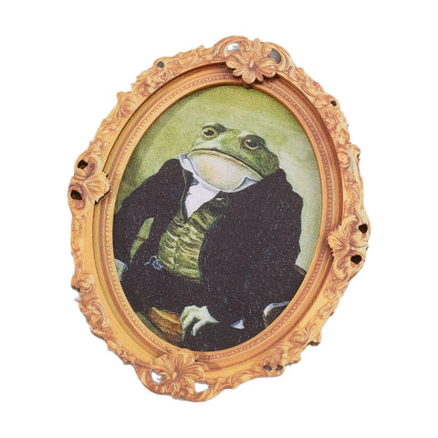 Gilt oval frame magnet holding a painted portrait of a frog in a black suit