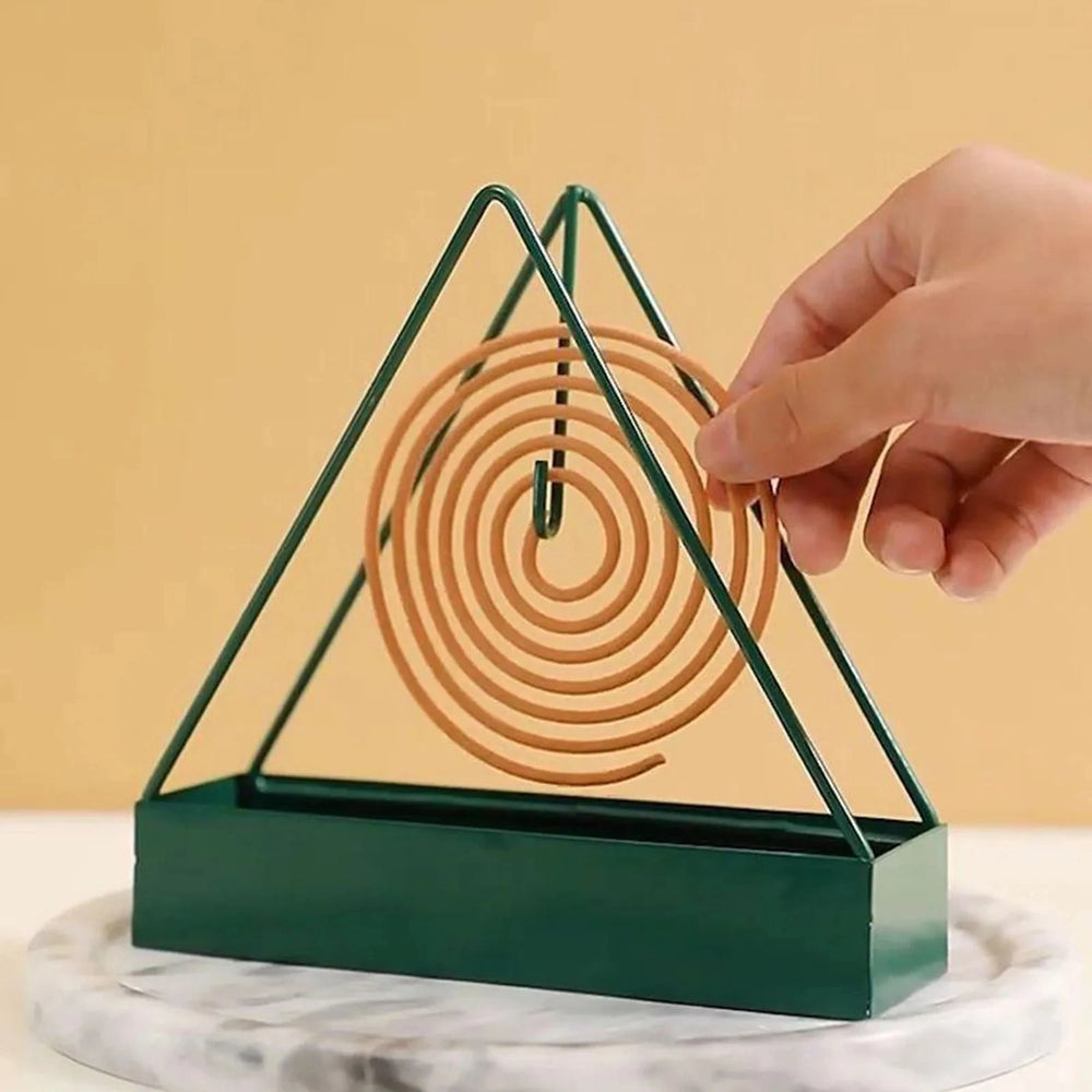 Green triangular metal mosquito coil holder on a marble coaster, with a spiral coil being hung on its hook - the coil is not included
