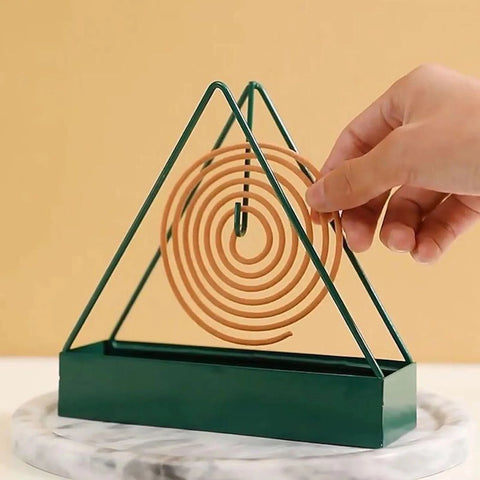 Green triangular metal mosquito coil holder on a marble coaster, with a spiral coil being hung on its hook - the coil is not included