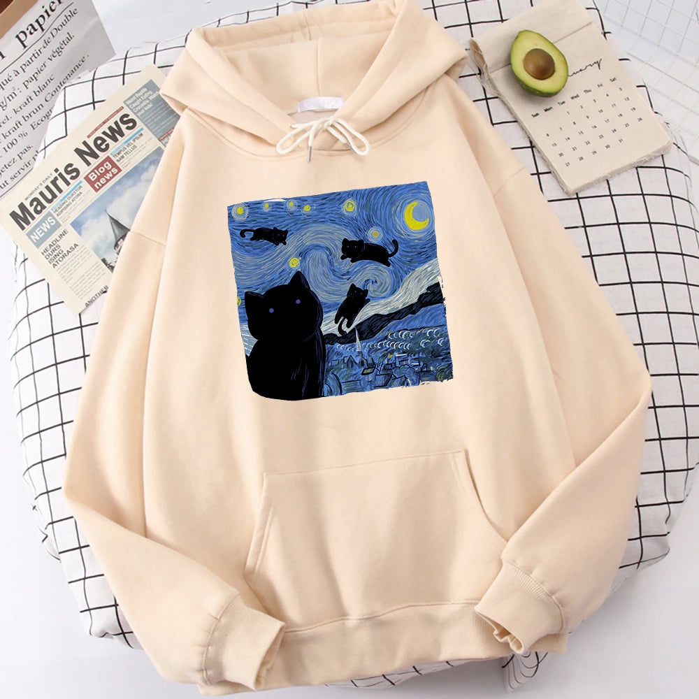 Beige fleece pullover hoodie with a large front print of a swirling starry night sky, a crescent moon and black cats over a village