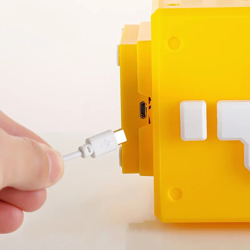 A hand holding a white micro-USB plug beside the matching micro-USB socket on the back of the cube