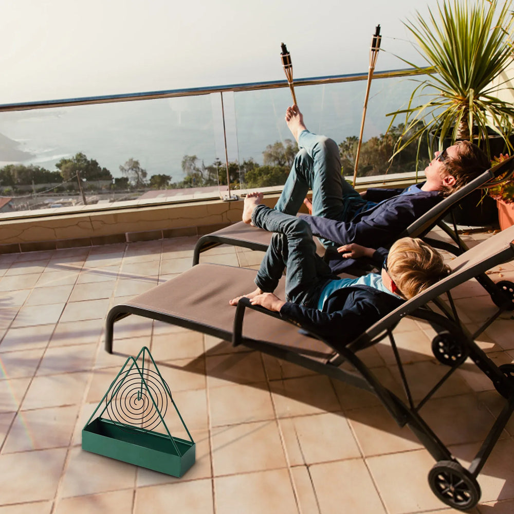 A green holder with a burning coil on a terrace floor - the lounger, garden torches and plants are not included