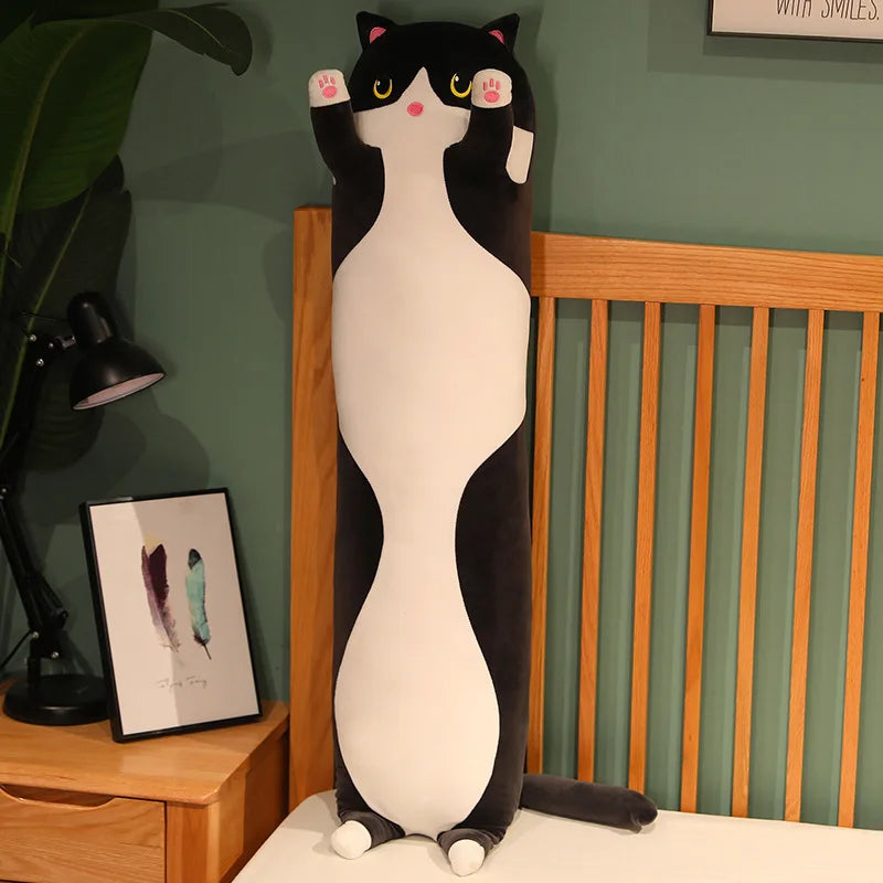 Black and white long cat body pillow standing upright against a bed frame