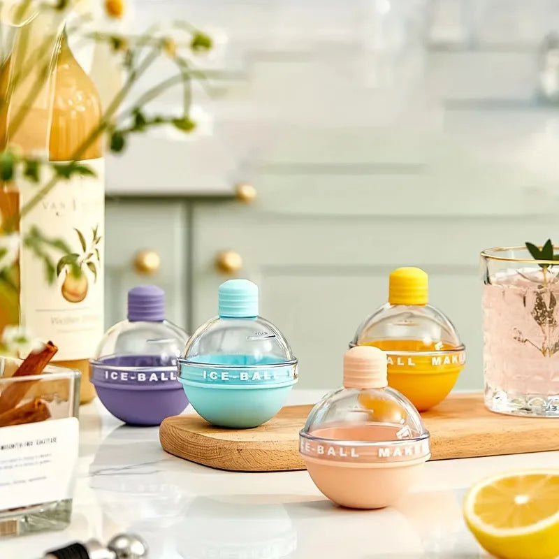 Four round ice ball molds lined up on a kitchen counter beside a bottle and a tall iced drink