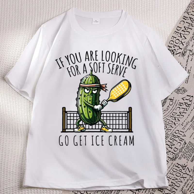 White pickleball tee laid flat, cartoon pickle with a paddle printed on the chest