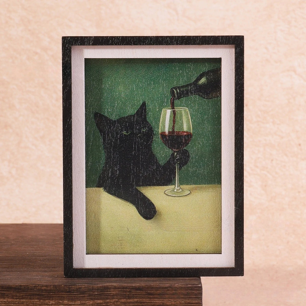 Black framed magnet holding a painting of a black cat being poured a glass of red wine