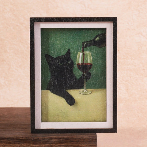 Black framed magnet holding a painting of a black cat being poured a glass of red wine