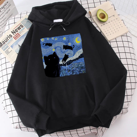 Black fleece pullover hoodie with a large front print of a swirling starry night sky, a crescent moon and black cats over a village