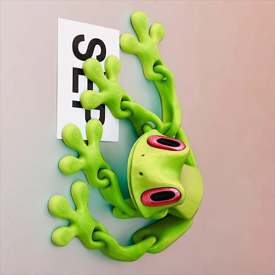 The green frog on a pale wall holding a white paper note