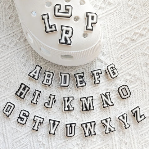 Alphabet letter shoe charms laid out beside a white foam clog with letters already fitted