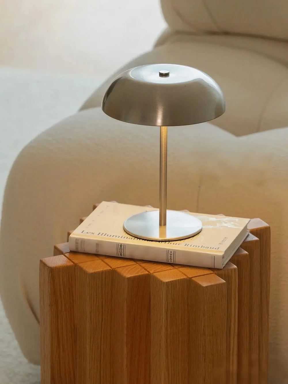 The silver lamp unlit on a wooden side table beside a book